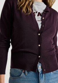 Mørklilla cardigan lavet af blødt strikket stof, med V-udskæring, fem knapper i guldfarve og ribbede manchetter, parret med lys denim.