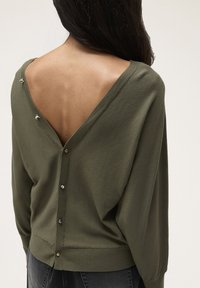 Pulover verde olivescu cu un design V la spate, având șase butoane decorative și manșete cu nervuri. Textură moale, croi relaxat și mâneci lungi.