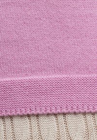 Rosa gestrickter Stoff mit glatter Textur, oben mit einem gerippten Rand. Darunter sorgt ein cremefarbener Zopfmuster für visuellen Kontrast.
