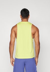 Õlavarteta ere kollane sportlik tank top, sile tekstuur, ümar kaelus, seljal on väike peegeldav aksent. Kombineeritud siniste lühikesed püksid.