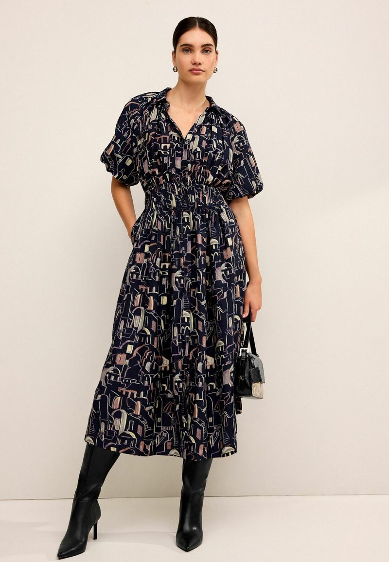 Rochie de lungime medie cu imprimeu floral, cu mâneci scurte tip puff, talie strânsă și bază de culoare bleumarin închis. Asortată cu cizme negre fitting până la genunchi.