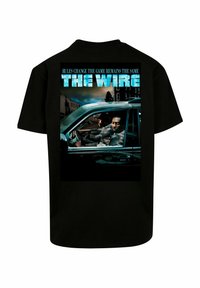 Svart bomull T-skjorte med grafisk trykk av en bilscene fra "The Wire," med blå tekst over som sier "REGLER ENDRES, SPIELLET FORBLIR DET SAMME."