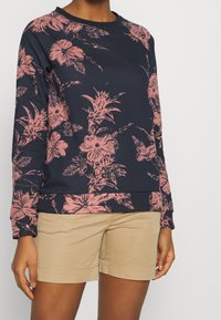 Felpa navy con motivo floreale rosa oversize, scollo a girocollo e orlo a costine. Abbinata a pantaloni corti beige, che mostrano uno stile casual.