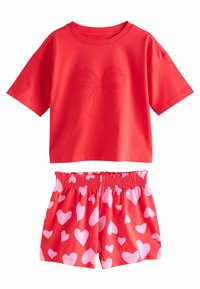 T-shirt rossa in cotone con un design a fiocco ricamato, abbinata a pantaloni corti rossi con un motivo a cuori rosa e vita elastica.