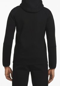 Sudadera negra con capucha y mangas largas, con una textura suave y diseño ajustado, vista desde atrás.