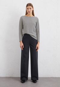 Striped long-sleeve top in gray and white, paired with wide-leg black trousers, featuring a smooth texture and relaxed fit.