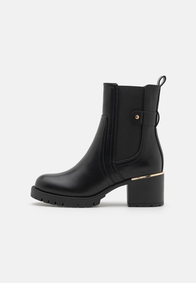 Bottine noire en cuir avec talon épais, panneau latéral élastique, languette de tirage et bride décorative avec clou doré et détail au talon.