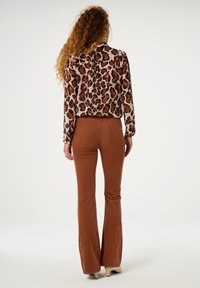 Brown flared pants gecombineerd met een blouse met een panterprint, voorzien van een gladde textuur en lange mouwen. De outfit toont rijke, warme kleuren.