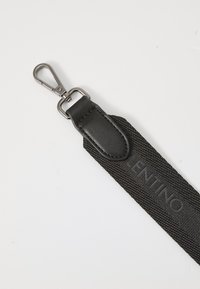 Svart tekstil snor med strukturert overflate, med lærdetaljer og en metallkrok for feste, som viser merkets navn.