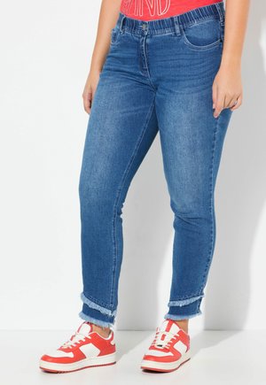 Modré džíny s slim fit střihem, s roztrhanými lemy a pětikilovými kapsami. V kombinaci s červenými a bílými teniskami.