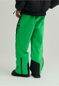 Pantalones impermeables verdes con acentos negros, corte relajado, bolsillos laterales con cremallera y dobladillo inferior reforzado para mayor durabilidad y funcionalidad.