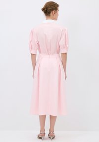 Abito rosa pallido con maniche a sbuffo, polsini con bottoni e colletto bianco. Presenta una cintura in vita e arriva fino a metà polpaccio. Tessuto liscio.