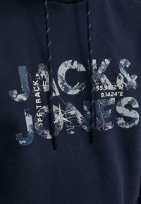Felpa con cappuccio blu navy con una grafica frontale in grigio chiaro e bianco, che mostra il testo "JACK & JONES" e le coordinate. Presenta un cordoncino.