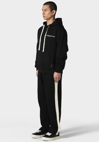 Svart hettegenser med hvite snorer og logo, sammen med svarte bukser med hvite side-striper, og svarte sneakers med hvite såler.
