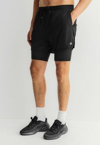 Sorte atletikshorts med snøre i taljen, der har et lagdelt design og en slank pasform nedenunder. Båret med sorte sportssko og hvide sokker.