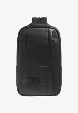 Mochila negra de cuero con acabado texturizado, cierre con cremallera y perfil delgado. Destaca por su marca visible y elementos de diseño minimalistas.