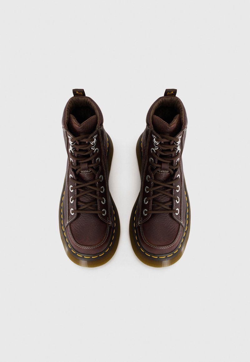 Bottes en cuir marron avec une finition texturée, six paires d'œillets, surpiqûres jaunes le long de la semelle, et un col rembourré pour le soutien.