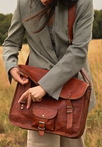 Braune Leder-Umhängetasche mit Klappe, Fronttasche und verstellbarem Schultergurt. Verfügt über Metallverschlüsse und eine strukturierte Oberflächenbeschaffenheit.