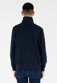 Felpa blu navy con colletto alto, realizzata in tessuto morbido. La vista posteriore mostra una texture liscia e una silhouette aderente.