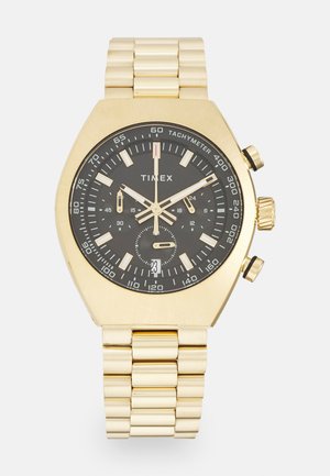 Montre chronographe dorée avec un cadran noir, un boîtier octogonal élégant, des accents argentés et un affichage de la date. Elle est dotée d'un bracelet en maillons métalliques.