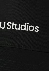 Schwarzer Hut aus strukturiertem Stoff mit dem weißen Schriftzug "AJ Studios". Abgerundeter Schirm mit nahtlosem Design und sichtbaren Nähten.