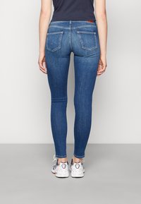 Jeans de mezclilla azul ajustados con bolsillos traseros, combinados con zapatillas blancas deportivas, con una camiseta corta y sin logotipos visibles.
