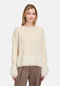 Cremefarbener Strickpullover mit strukturiertem Muster, ausgestattet mit einem flauschigen, fransigen Saum und Bündchen. Weiches Material mit langen Ärmeln.
