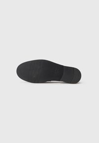 Schuhsohle aus schwarzem Gummi, mit einer glatten Oberfläche und drei horizontalen Rillen für besseren Halt, entworfen mit einem kleinen Absatz für Stabilität.