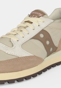 Μπεζ και ανοιχτό καφέ αθλητικό παπούτσι Saucony Jazz με κρεμ κορδόνια, πάνελ από σουέτ και ύφασμα και μια αυλακωτή σκούρα καφέ σόλα.