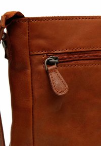 Ruskea nahkakäsilaukku, jossa on teksturoitu pinta, varustettuna vetoketjullisella taskulla ja ompeluyksityiskohdilla. Hopeanvärinen metallivetoketjun veto.