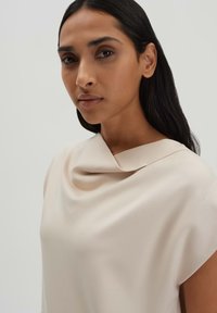 Beige Drapierter Top aus weichem Stoff, mit weitem Ausschnitt und kurzen Ärmeln. Glatte Textur mit minimal sichtbaren Nähten.