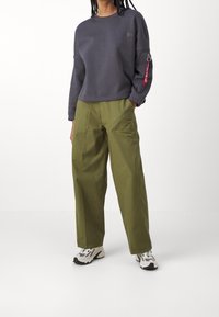 Tmavě šedá mikina s krátkým střihem, elastickými manžetami a červenou visačkou na rukávu, doplněná širokými olivově zelenými kalhotami.