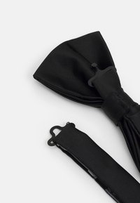 Schwarze Fliege aus strukturiertem Stoff, mit einem glatten, verstellbaren Band. Auffälliges Detail: ein Verschluss mit dekorativem Design.