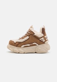 Sneaker marrone in suede con rivestimento bianco soffice, suola chunky beige e lacci metallici. Presenta un logo sul tallone e una parte superiore testurizzata.