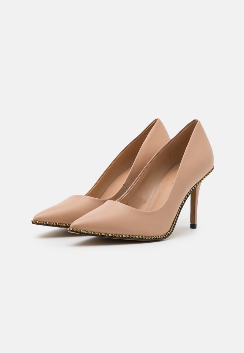 Décolleté in pelle nuda con punte affusolate, dettagli rivestiti di borchie dorate lungo le suole e sottili tacchi a spillo neri.