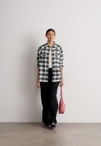 Camisa de cuadros en blanco y negro con botones, pantalones anchos negros y un bolso de hombro rosa. Textura suave, diseño clásico, cuatro bolsillos frontales.