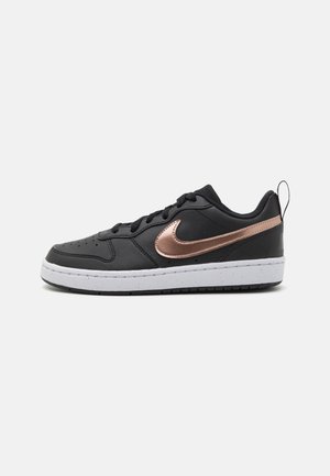 Baskets noires en cuir avec une semelle intermédiaire blanche, présentant un swoosh Nike rose doré et des lacets noirs, une pointe arrondie et une languette au talon.