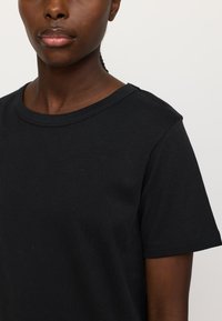 Black cotton t-shirt with a round neckline and short sleeves. The fabric appears smooth with a slight stretch.