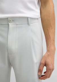 Pantalons en gris clair texturé avec un pli avant, fermeture à un seul bouton et taille ajustée. Le tissu présente un motif tissé subtil.
