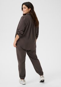 Chemise brune à manches longues, ample et décontractée, assortie à un pantalon. Texture douce, design casual, avec une taille élastique et des poignets élastiques.