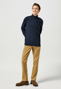Granatowy sweter z golfem z prążkowanym kołnierzem, w połączeniu z khaki spodniami z korduru i brązowymi mokasynami. Gładka faktura, dopasowany krój.