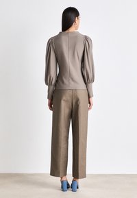 Haut marron ajusté avec des manches ballon, associé à un pantalon large taille haute. Les chaussures présentent des talons carrés bleus. Texture lisse.