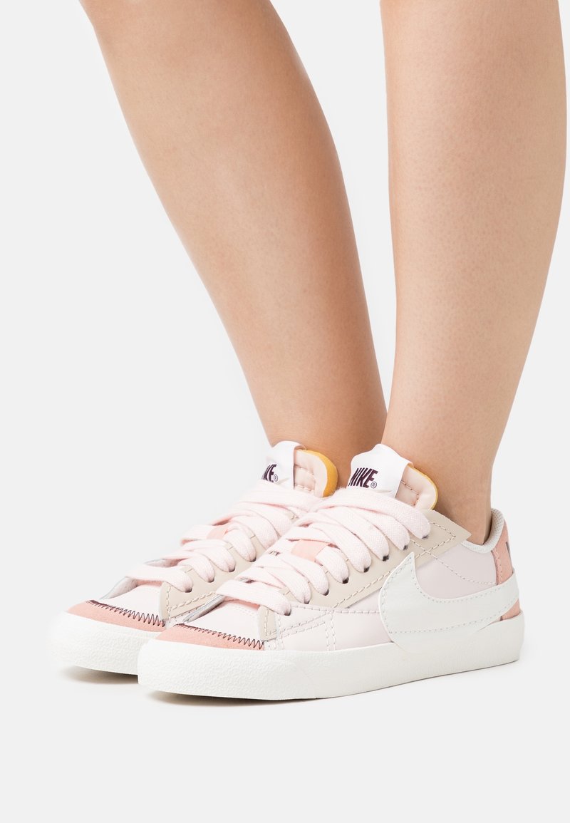 Ljusrosa sneakers med vita accenter och gummisulor. Rundad design, platta snören och minimala sömdetaljer. Nike-logotyp på tungan.