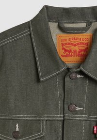 Mörkgrön denimjacka med kontrasterande vit sömnad, klassisk krage och en Levi Strauss & Co. etikett på den inre halslinningen.