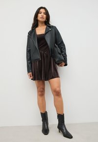 Črna usnjena jakna čez temno žametno poletno obleko z nabranim pasom, kombinirana s črnimi gležnjaki z zadrgo.