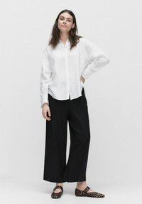 Witte linnen button-up shirt gecombineerd met losse zwarte broeken en flats met luipaardprint. Heeft een relaxte pasvorm en lange mouwen.