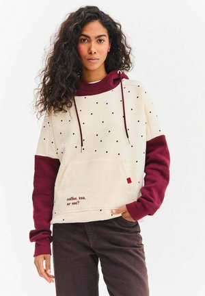 Kremowa bluza z kapturem z bordowymi rękawami, ozdobiona wzorem w kropki i przednią kieszenią. Na kieszeni napis: „kawa, herbata czy ja?”