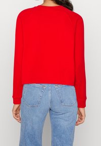 Czerwony sweter z długimi rękawami i okrągłym dekoltem, z krótkim rękawem i ściągaczami. Zestawiony z jasnoniebieskimi dżinsami.