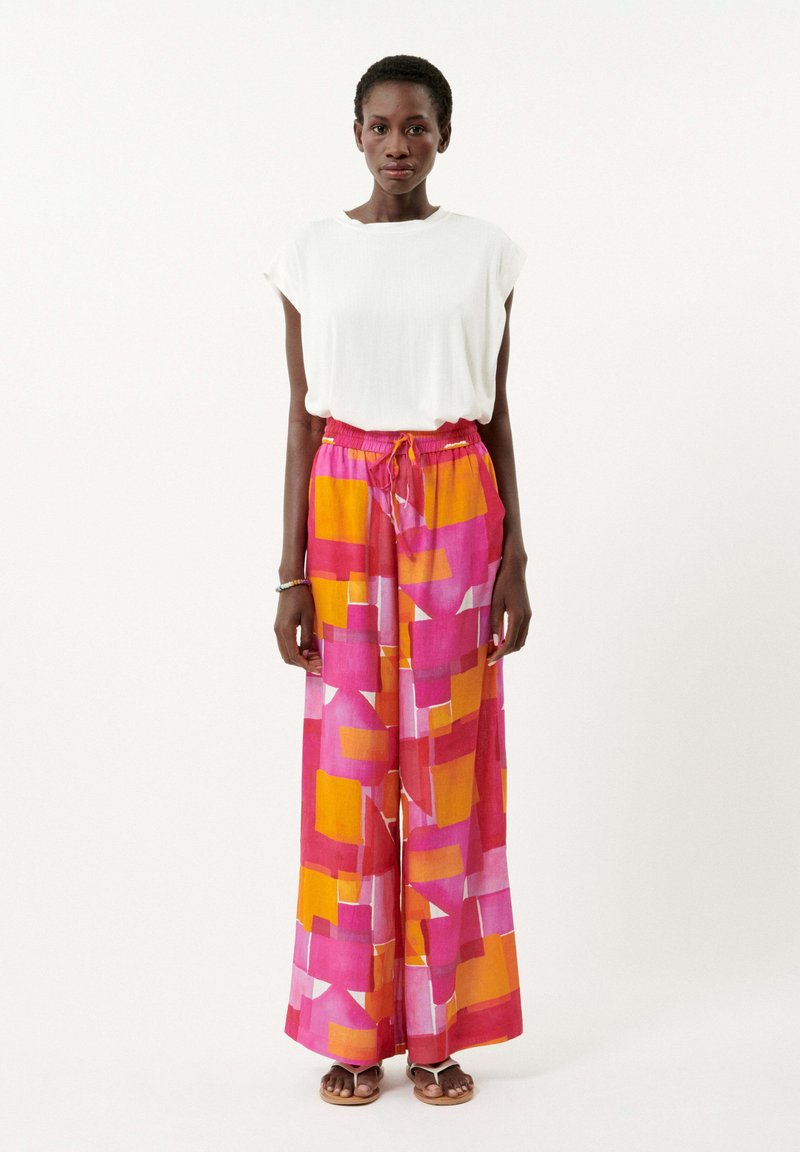 Haut blanc à manches courtes associé à un pantalon large à motifs en formes géométriques roses, orange et jaunes ; tissu léger et taille à cordon.