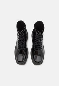 Black patent leather ankle boots with a smooth finish, featuring laces, zippers, and a textured rubber sole.